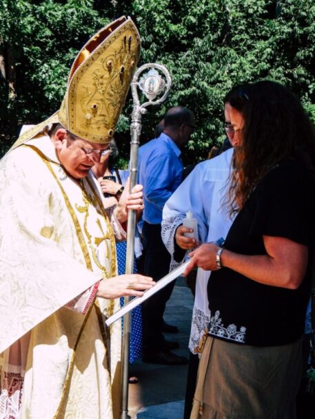 Cardinal Burke Blessing Cardinal Raymond Burke offering a blessing to a woman holding a religious item during an outdoor event.